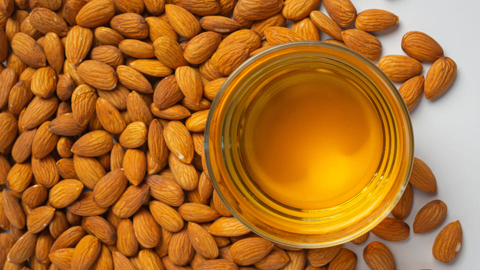 Almonds around a bowl of cold-pressed almond oil